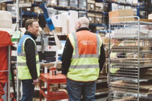 Top fulfillment mistakes and how to avoid them: image shows two workers in high vis jackets standing in a busy warehouse.